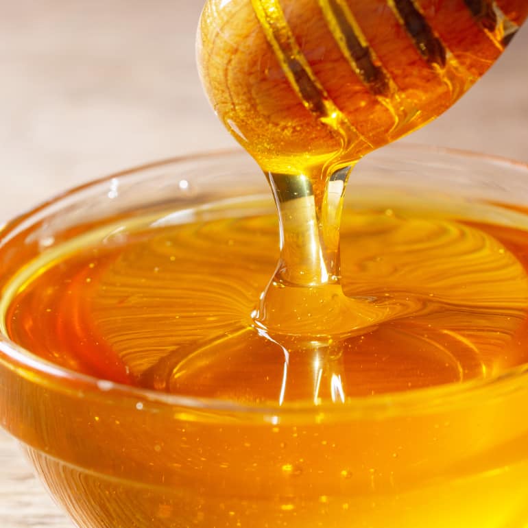 A honey wand dripping golden honey into a glass bowl.
